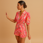 Women’s short summer jumpsuit with vibrant print and waist belt, available in pink and purple, perfect for warm days and summer outings.